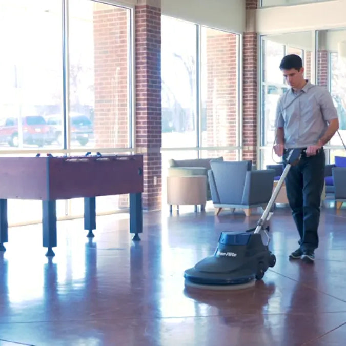 Operator running a Powr-Flite floor burnisher across a glossy, reflective lobby floor beside tall windows