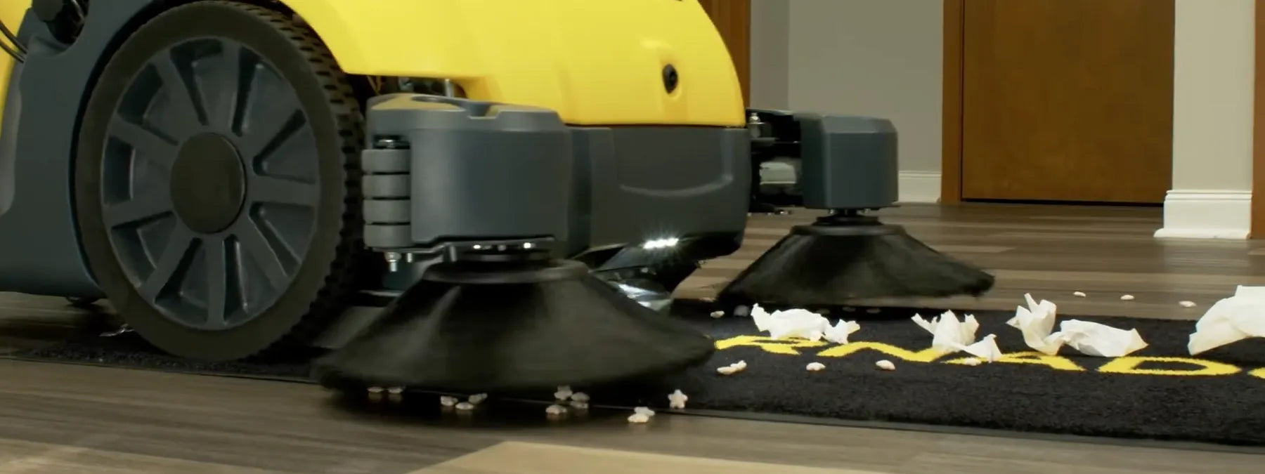 Low close-up of a Tornado Torrent walk-behind sweeper whose side brooms sweep popcorn and paper scraps off the floor