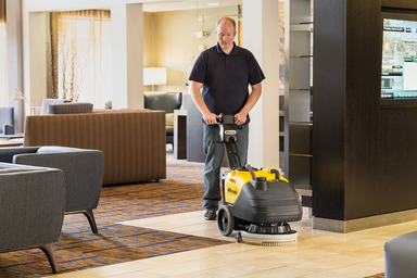 A man using the Tornado BD 14/4 Compact Cordless Auto Scrubber to clean a hotel lobby floor