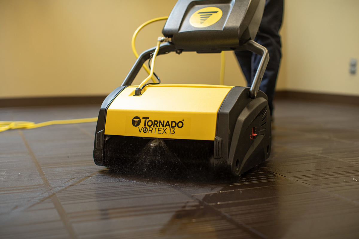 Tornado V13 Multi-Surface Scrubber In Use Cleaning a Room. In the front you can view it working and spraying the cleaning solution on the floor.