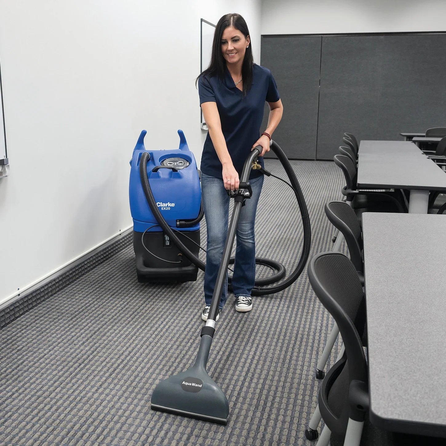 Cleaning technician extracting office carpet with the Clarke EX20 scrub wand, the machine parked behind her