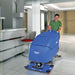 Operator pushing a Clarke Focus II BOOST 28 scrubber across a tile floor in a modern office
