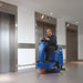 Operator scrubbing an elevator lobby floor with a Clarke Focus II MicroRider, next to the steel elevator doors