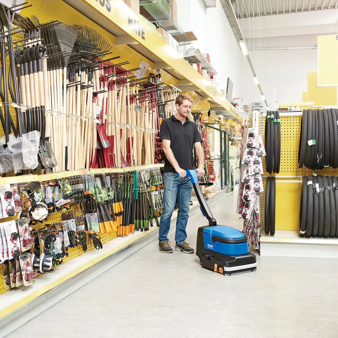 Operator scrubbing a hardware store aisle with the Clarke MA30 13B battery micro scrubber