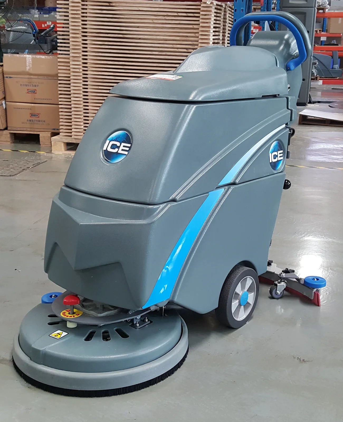 ICE i18C floor scrubber parked on a sealed concrete warehouse floor next to stacked pallets and boxes