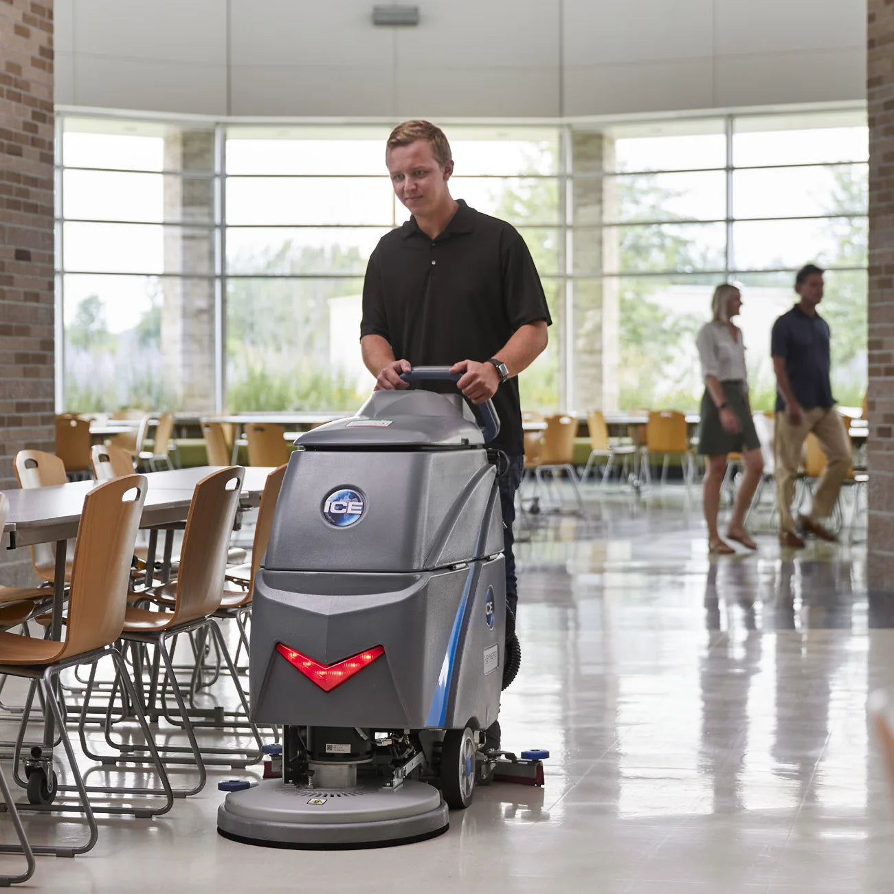 Operator walking behind an ICE i20NBTL+ floor scrubber across a shiny cafeteria floor