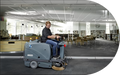Operator riding the ICE iS1100L+ floor sweeper across an open commercial interior with glass partitions