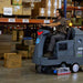 Operator driving the ICE RS28L-CY down a warehouse aisle, scrubbing the concrete floor between pallet racks