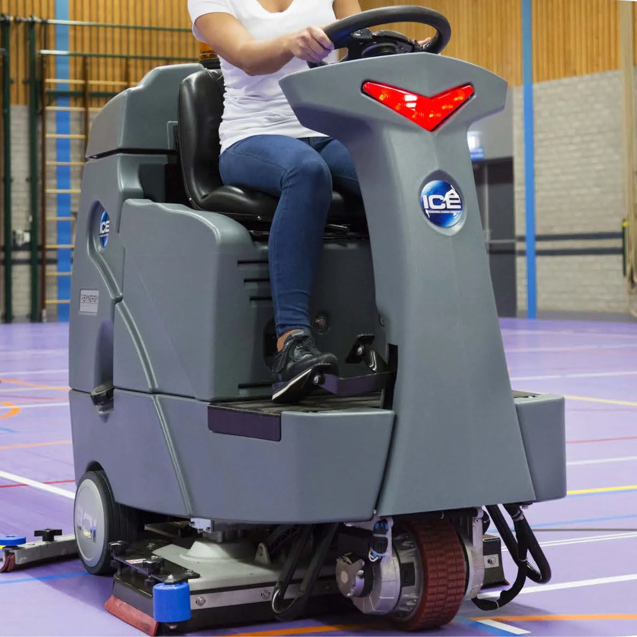 Operator driving an ICE ride-on floor scrubber across a large indoor floor