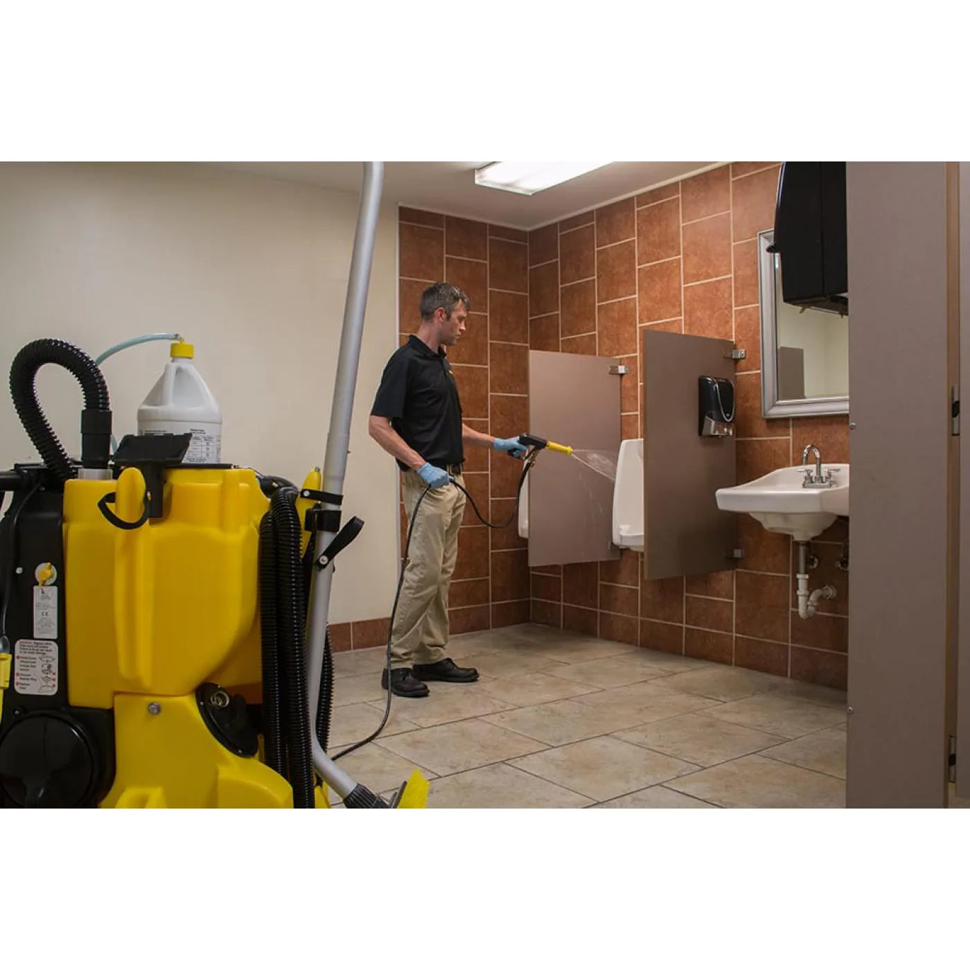Operator spraying cleaning solution onto a restroom wall with the KaiVac 1250 parked nearby