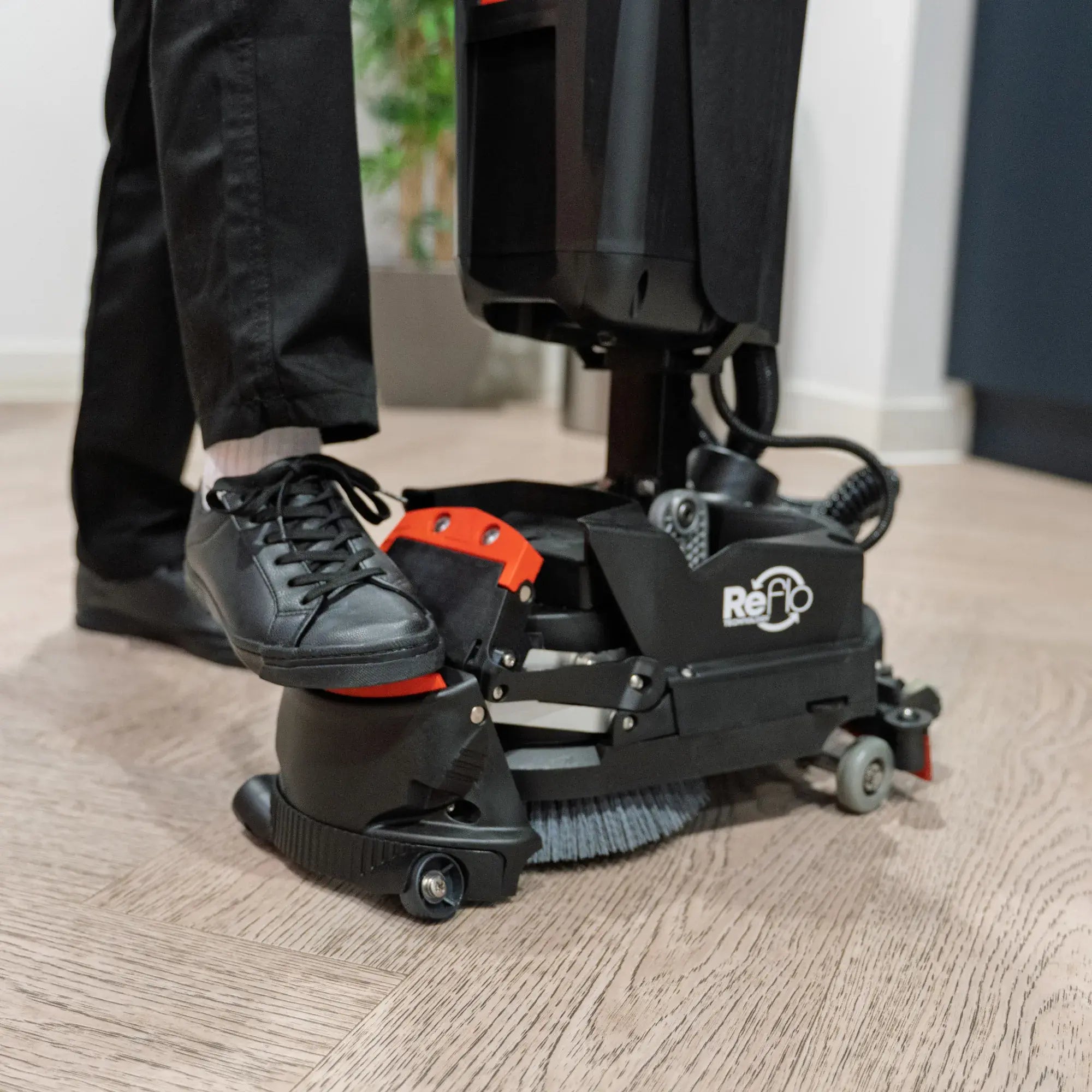 Operator's foot pressing the red 220NX deck pedal to lower the brush and squeegee on a wood-look floor