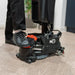 Operator's foot pressing the red 220NX deck pedal to lower the brush and squeegee on a wood-look floor