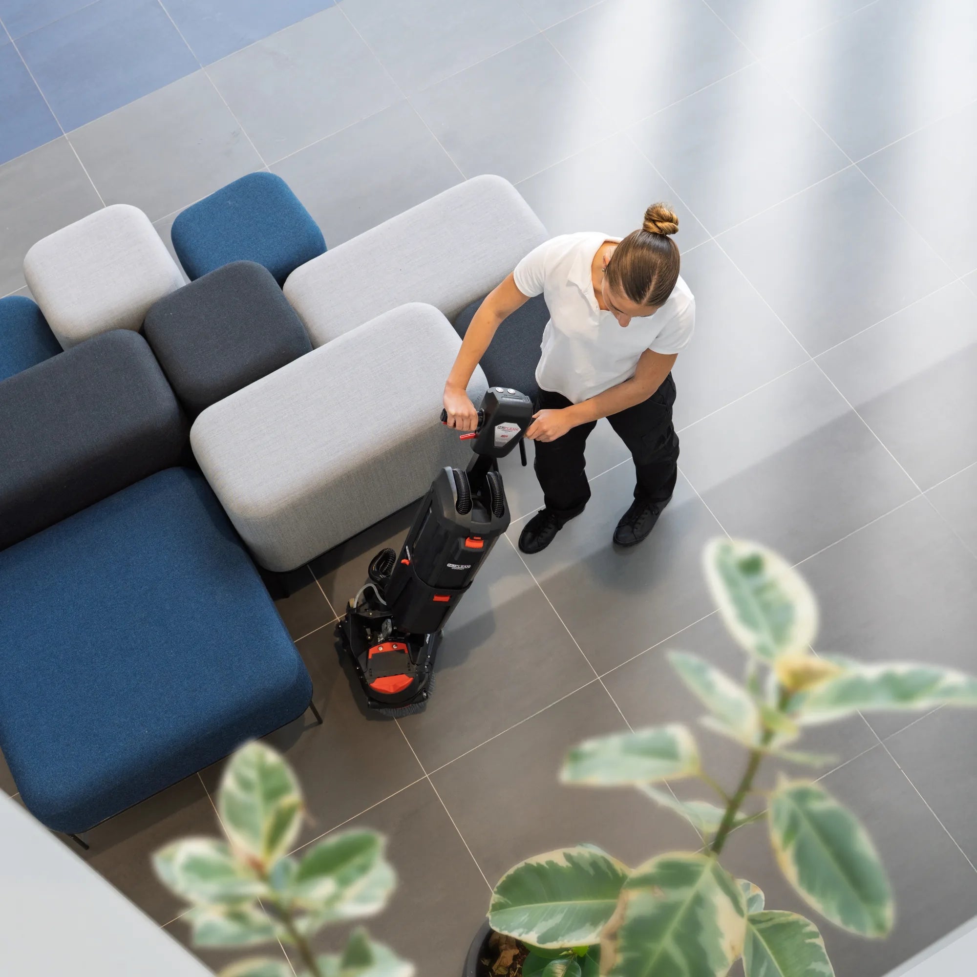 Overhead view of an operator steering the 220NX around lobby sofas on a gray tile floor