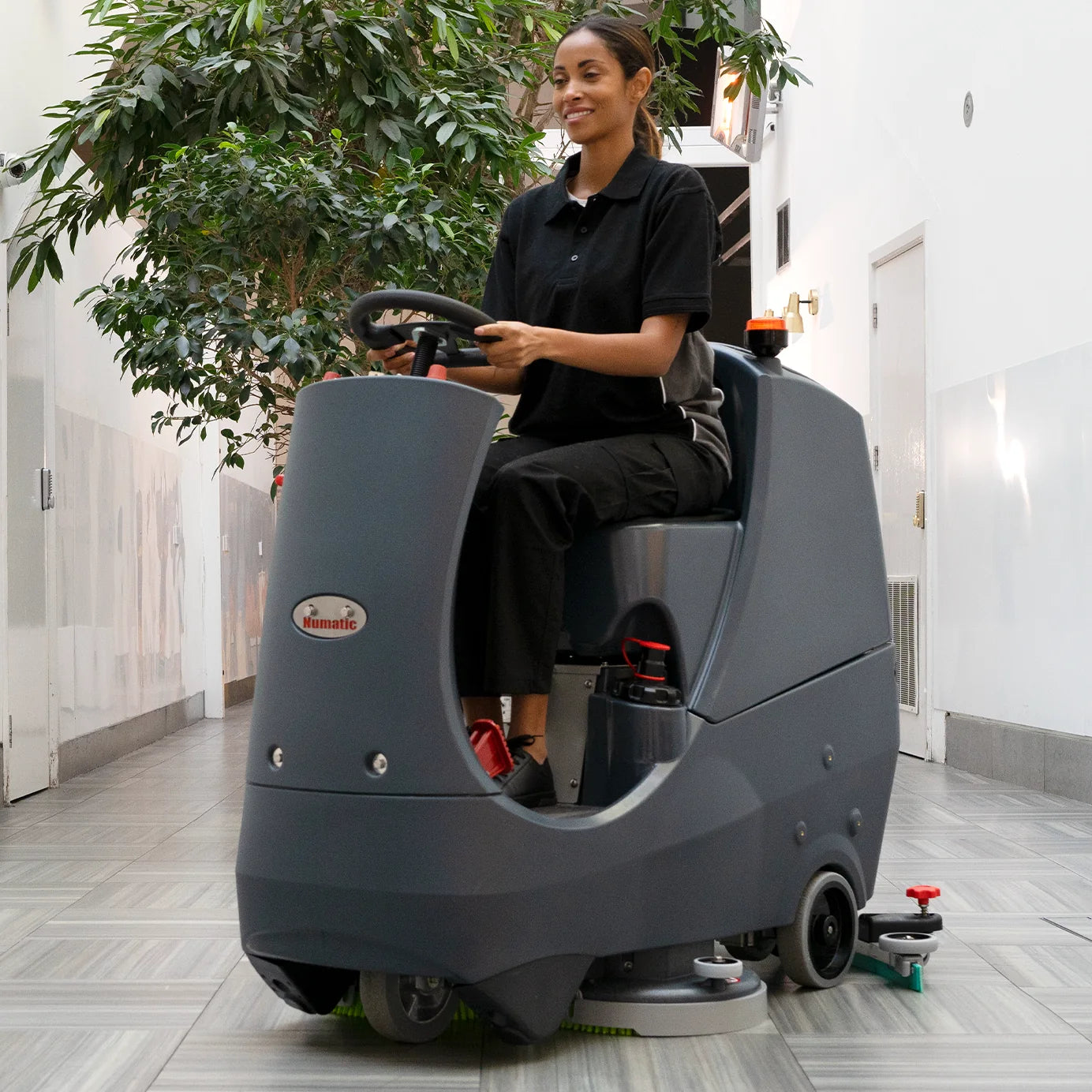 Operator driving the NaceCare CRL 2128 ride-on scrubber down a hallway