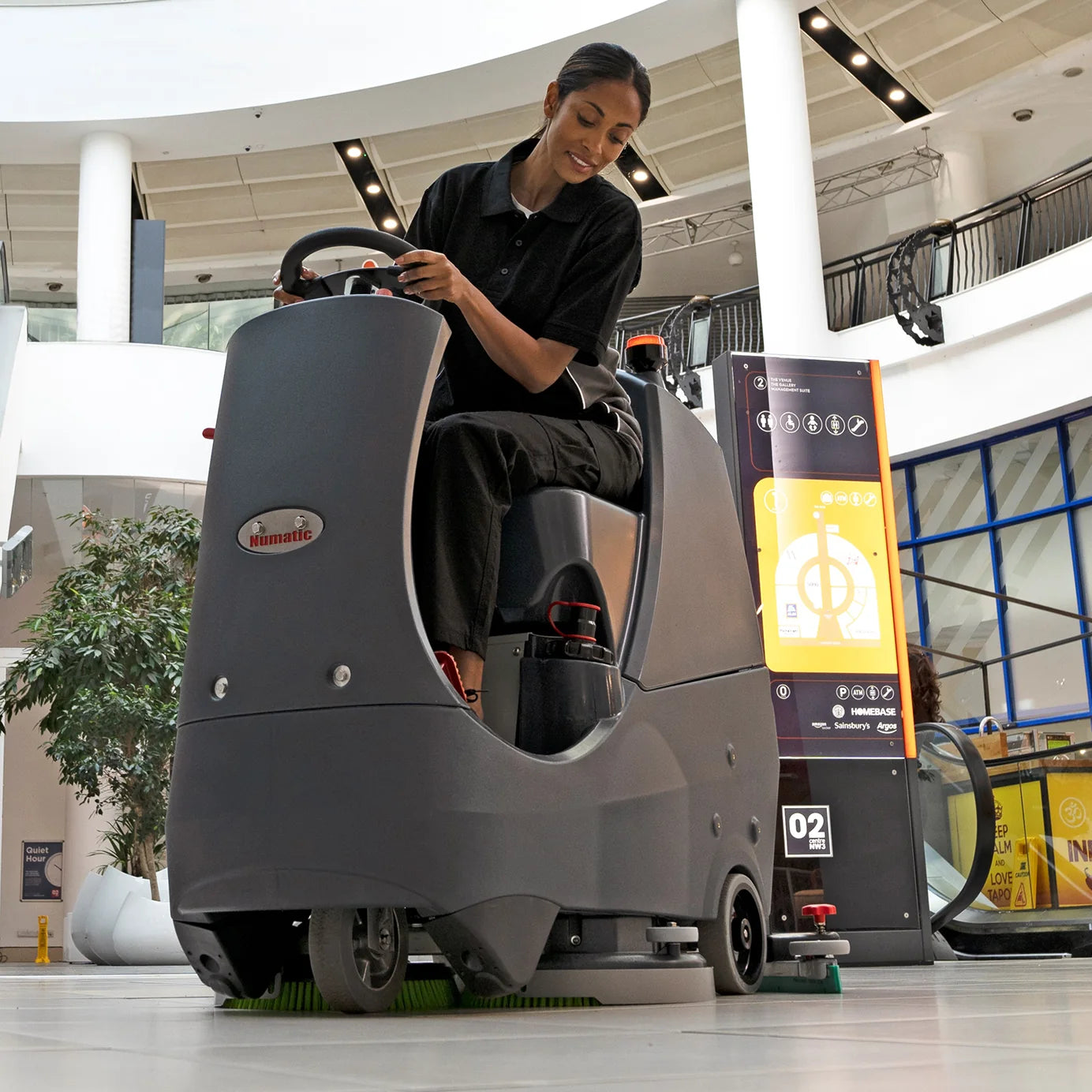 Operator driving the NaceCare CRL 2128 ride-on scrubber across a large indoor floor
