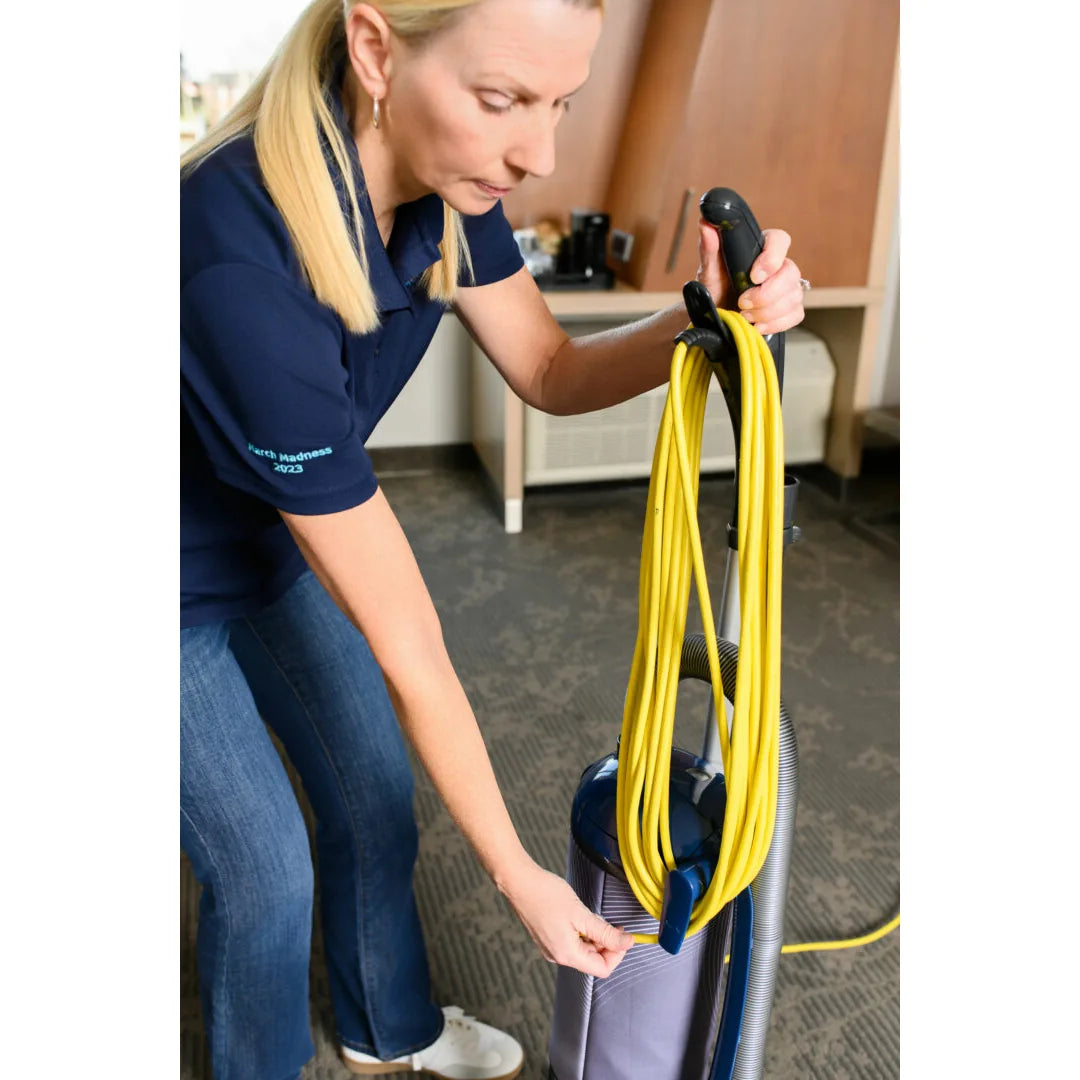 Housekeeper wrapping the yellow 40-foot cord on the NaceCare upright vacuum