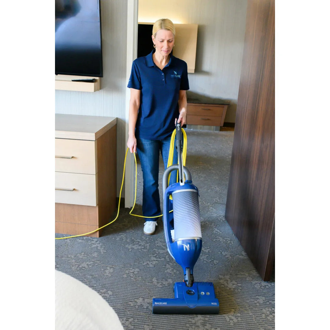 Housekeeper vacuuming beside the bed in a hotel room with a NaceCare upright