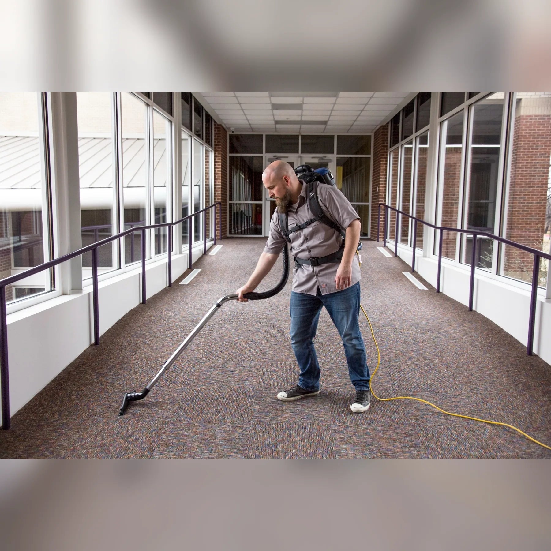 Cleaner vacuuming a carpeted glass walkway with a Comfort Pro backpack vacuum