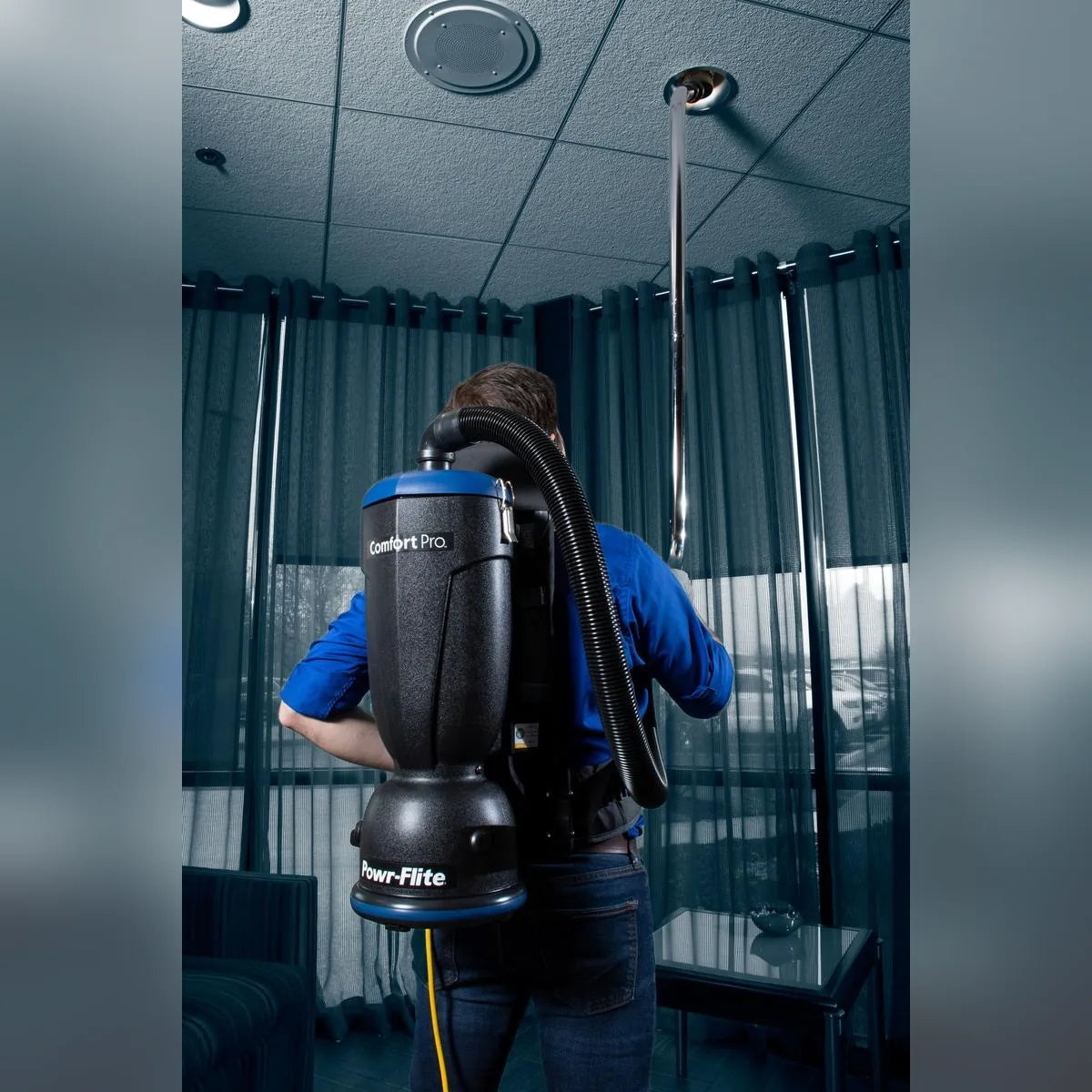 Operator reaching the ceiling of an office with the wand of a Comfort Pro backpack vacuum