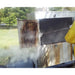 Steam cleaning the greasy interior of a commercial smoker oven outdoors with a long wand