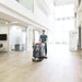 Operator guiding a Viper AS5160 floor scrubber across a light wood-look floor in a bright office atrium