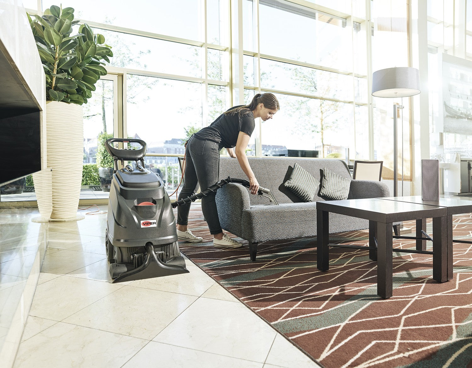 Operator cleaning a lobby sofa with the hose and hand tool of a Viper CEX410 carpet extractor